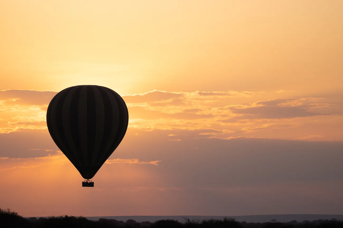 A hot-air balloon silhouetted against an orange sunrise over the plains