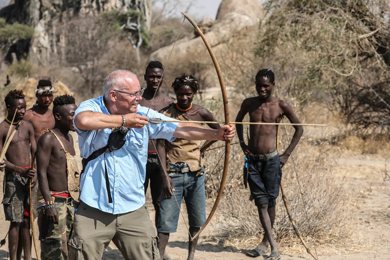 A guest drawing a Hadzabe bow, watched by Hadzabe men holding their own bows
