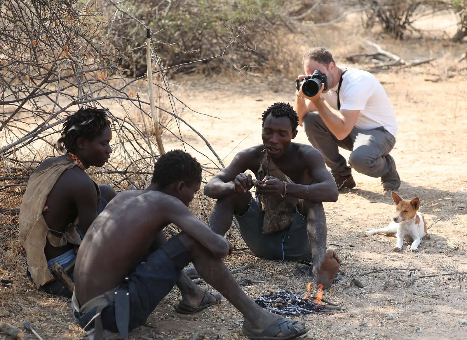Hadzabe men lighting a fire by hand while a guest photographs them
