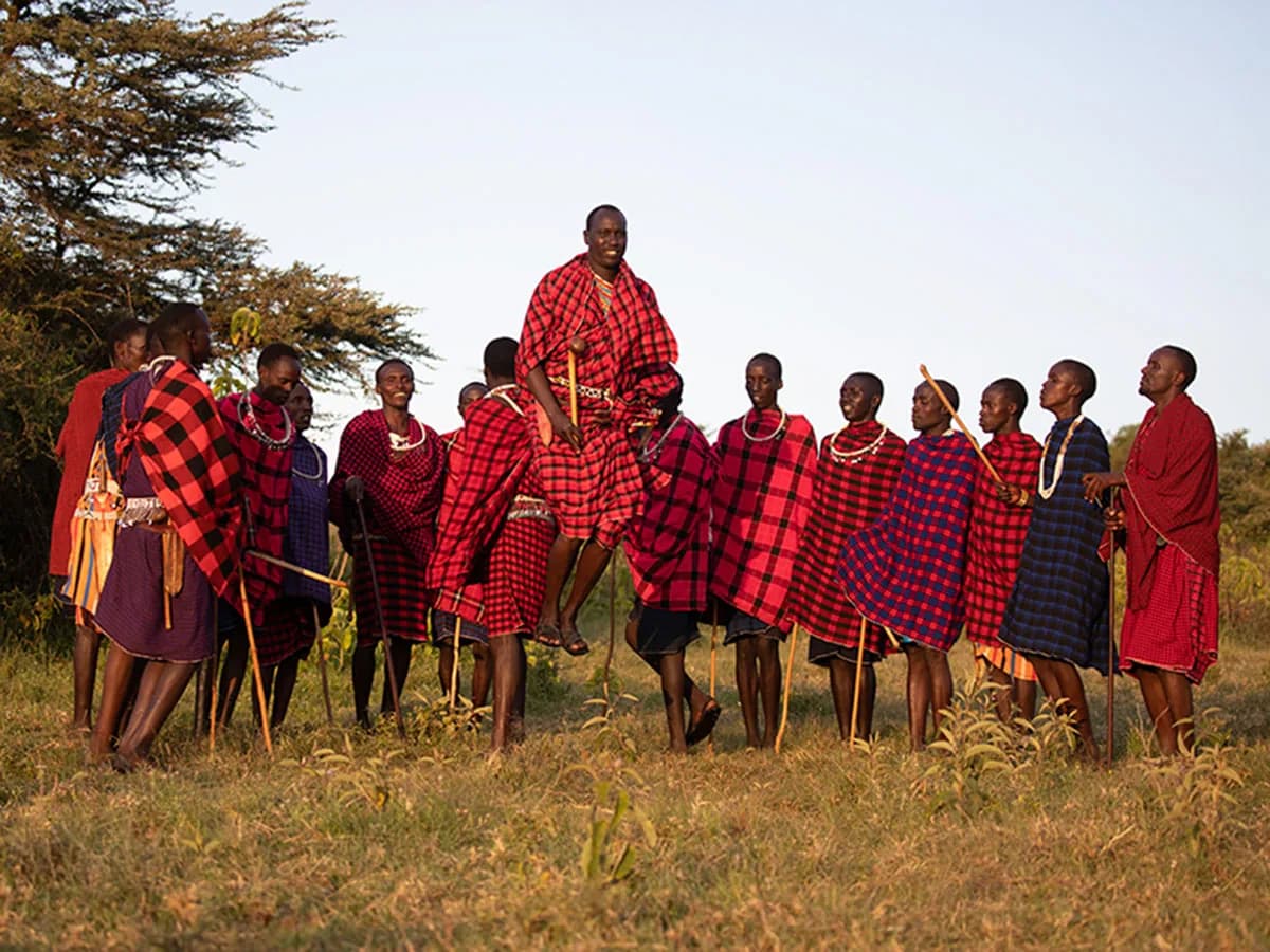 A line of Maasai in red and purple shukas, one man leaping high in the jumping dance