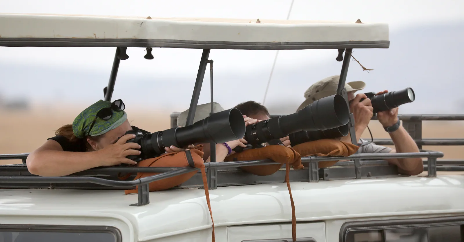 Guests leaning out of a safari vehicle's open roof with long telephoto lenses