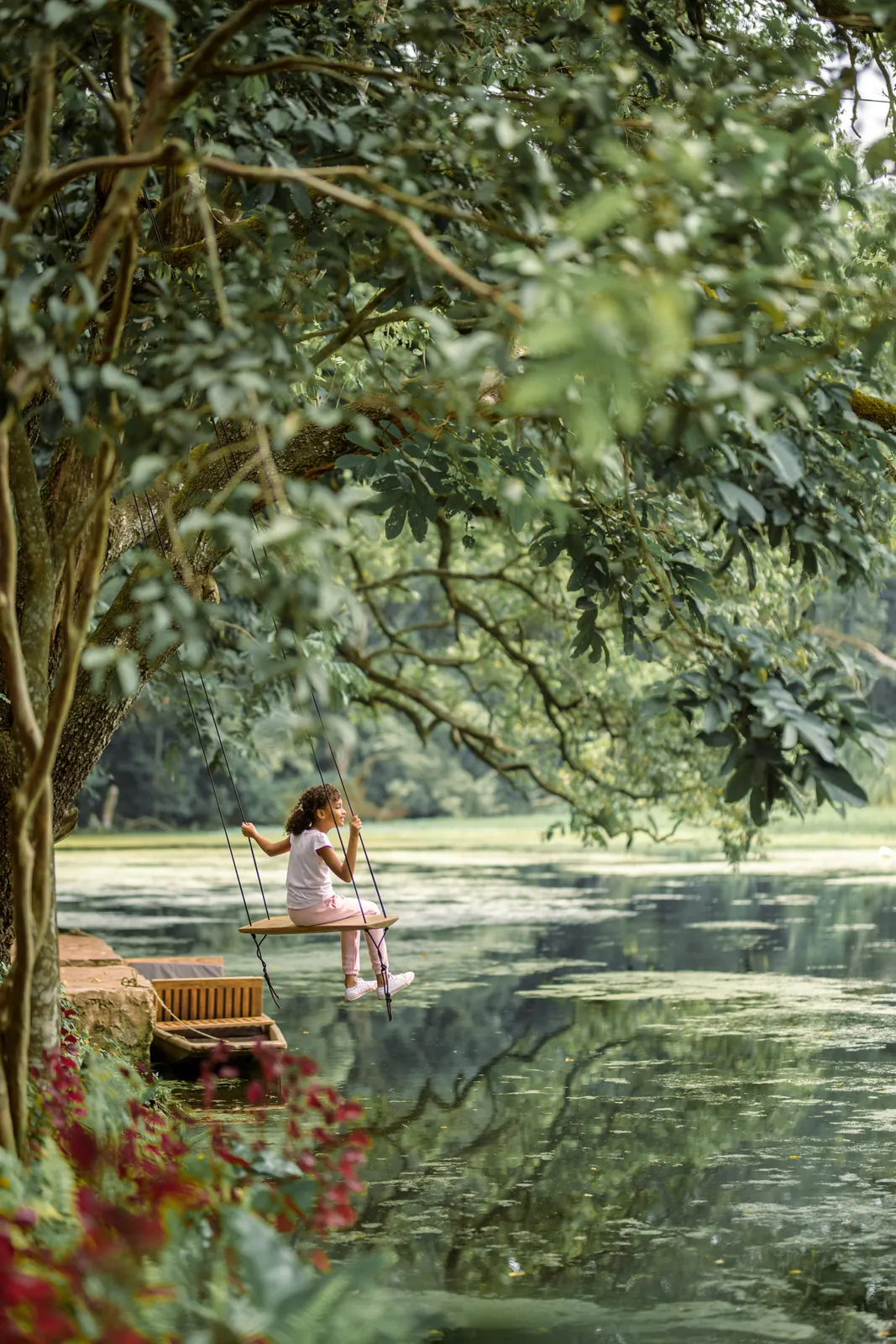 A girl sitting on a rope swing under a tree at the edge of a lake