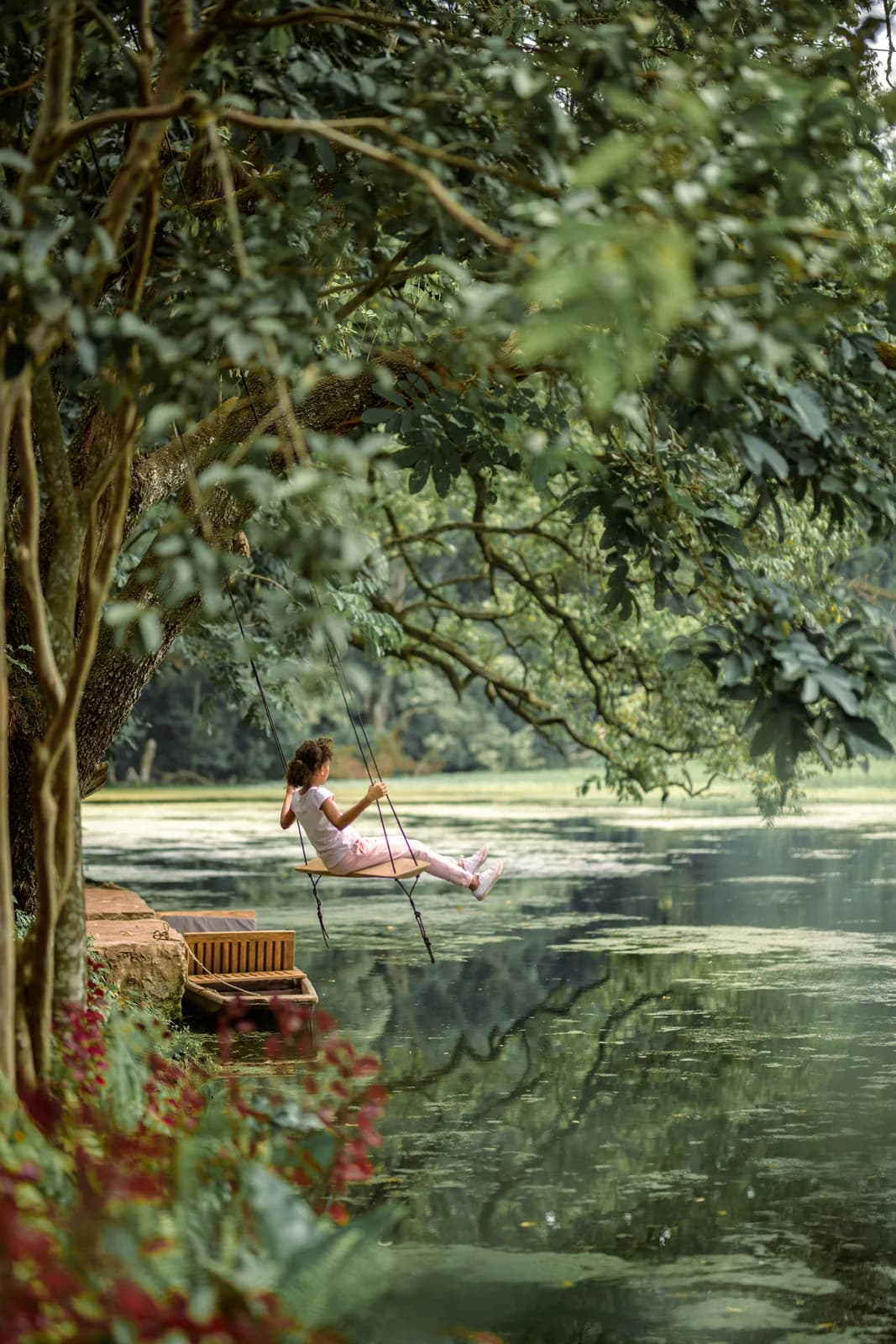 A girl on a rope swing hanging from a tree, swinging out over a lake