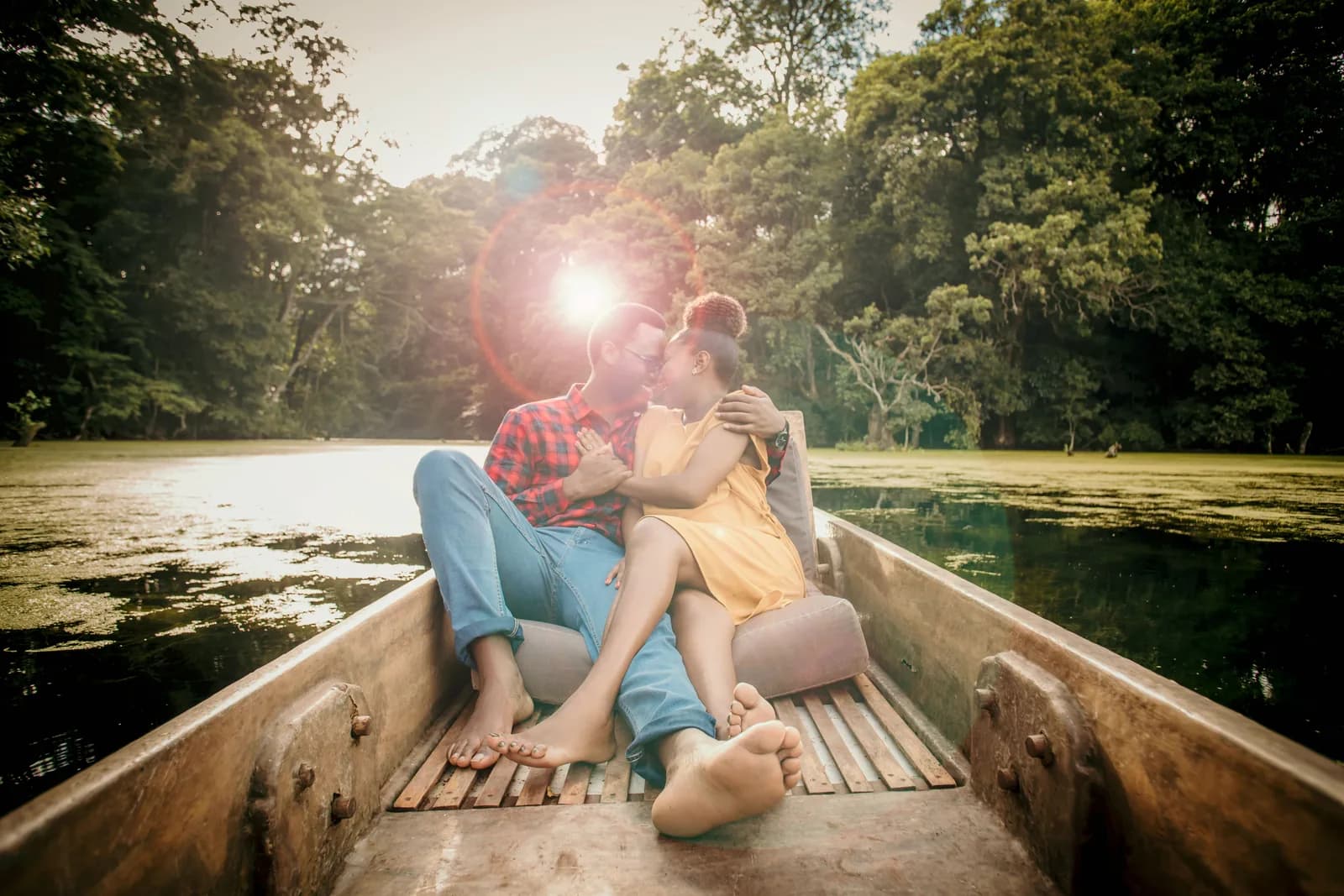 A couple kissing in a wooden canoe on a forest lake, the low sun shining through the trees behind them