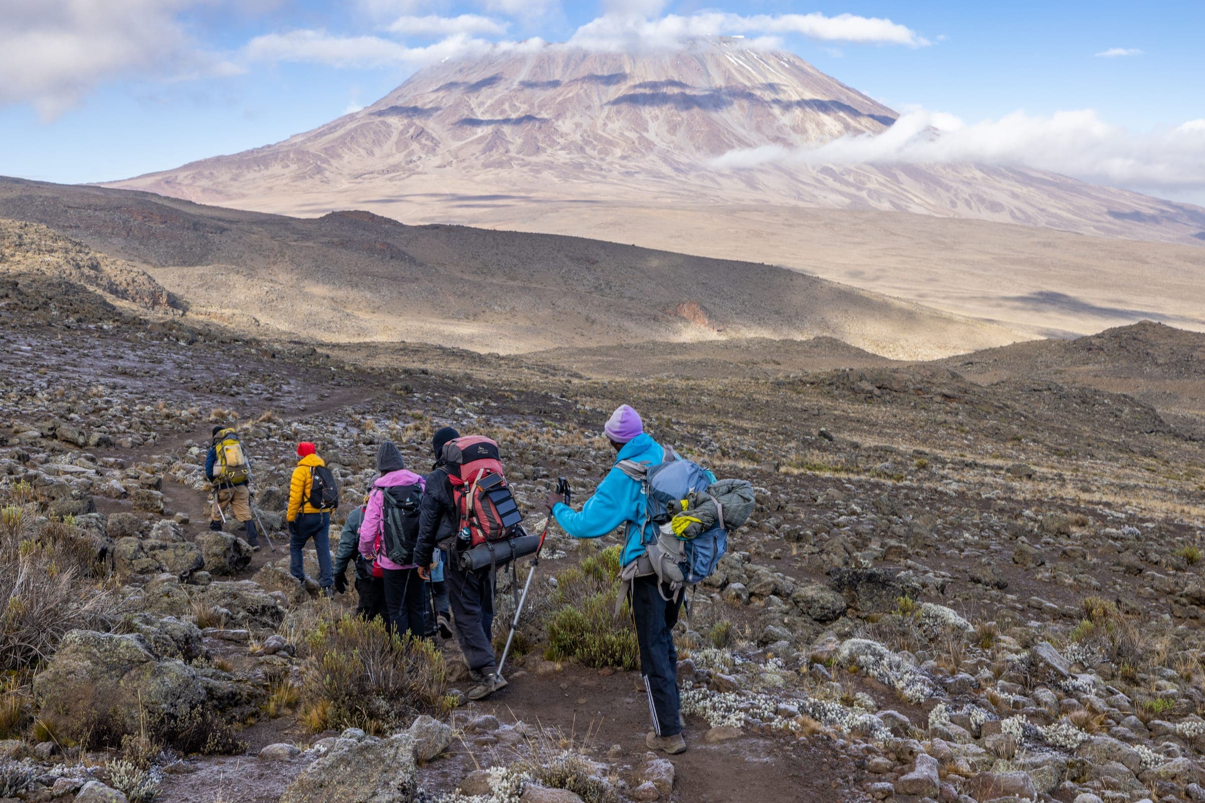 Trekkers with backpacks and poles crossing rocky alpine desert below the mountain