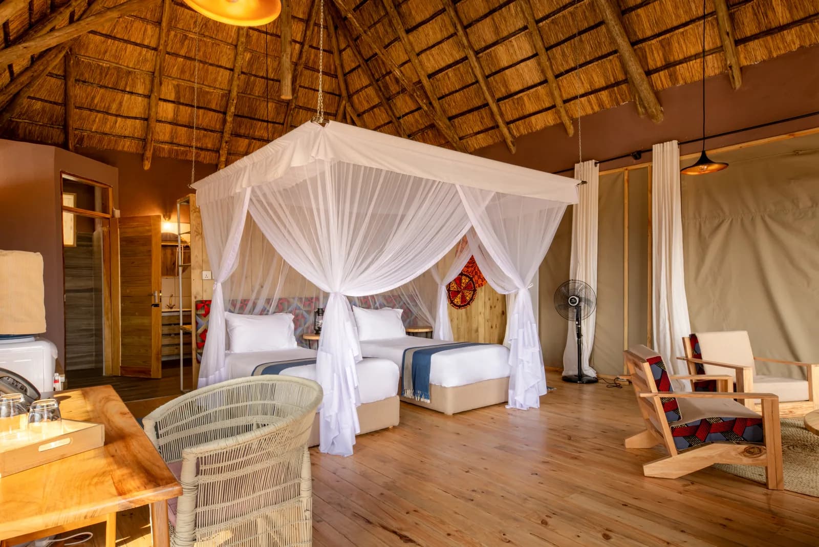 Twin beds under a netted canopy in a thatched room with a wooden floor