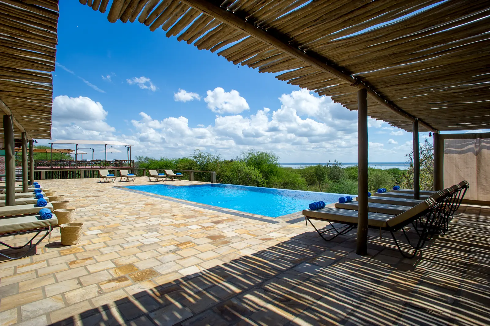 Swimming pool and loungers seen from a shaded reed-roofed terrace