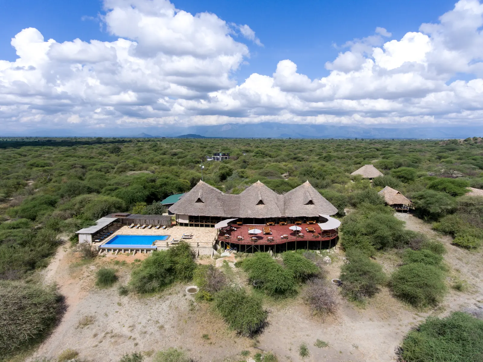 Aerial view of the thatched main lodge and pool in green bush, with Lake Burunge beyond