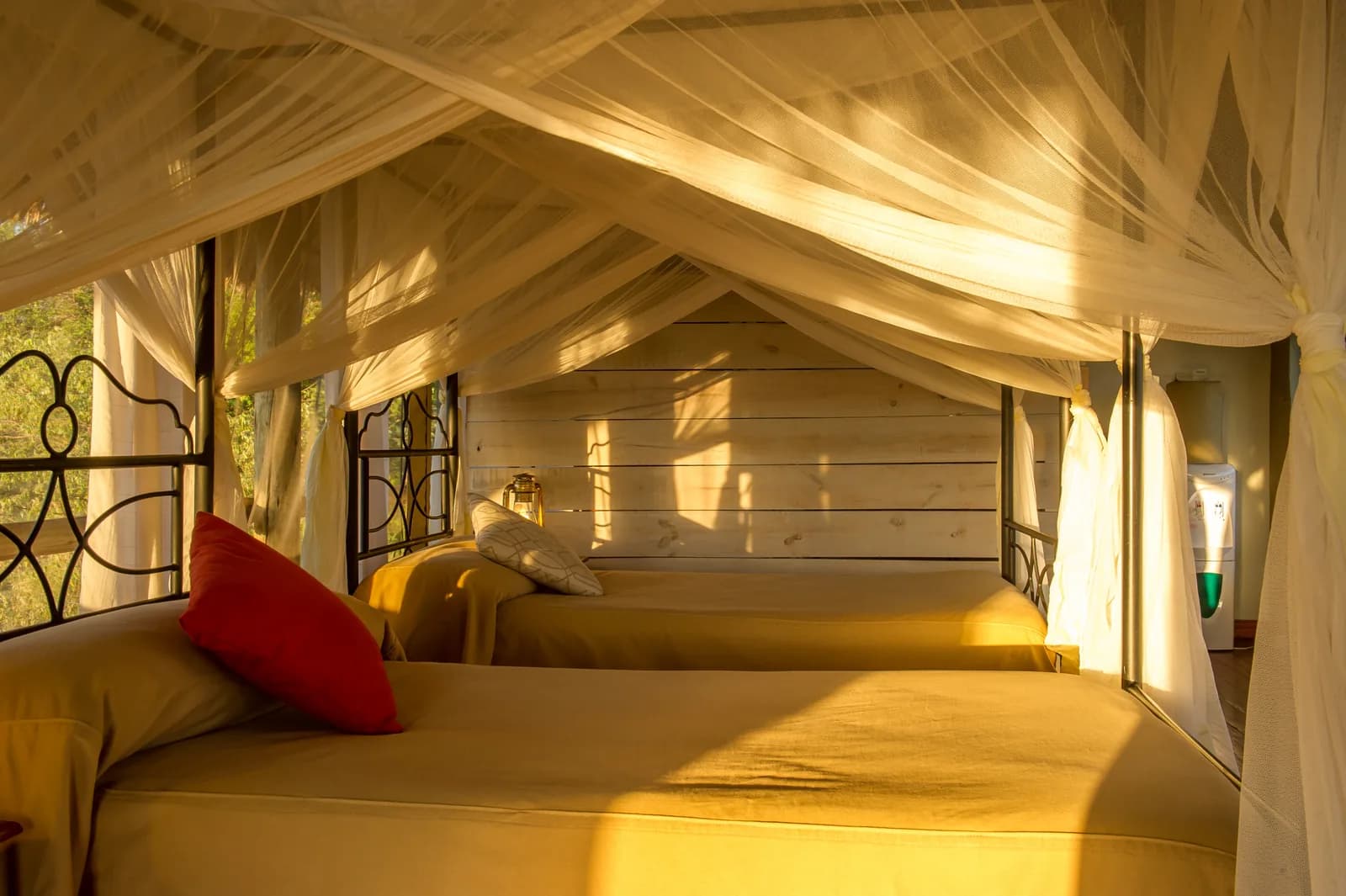 Twin beds under a mosquito net in a tent lit by warm afternoon sun at Burunge Tented Lodge