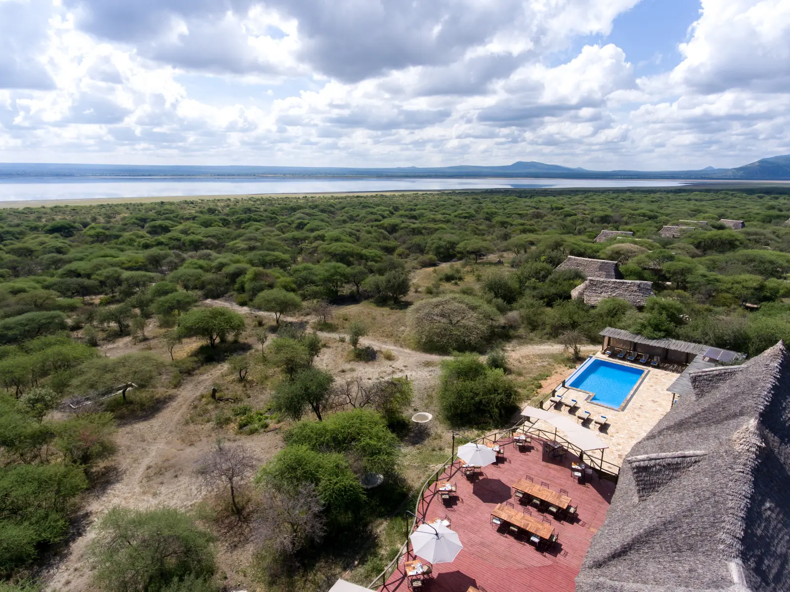 Aerial view over the pool deck and thatched roofs across bushland to the lake
