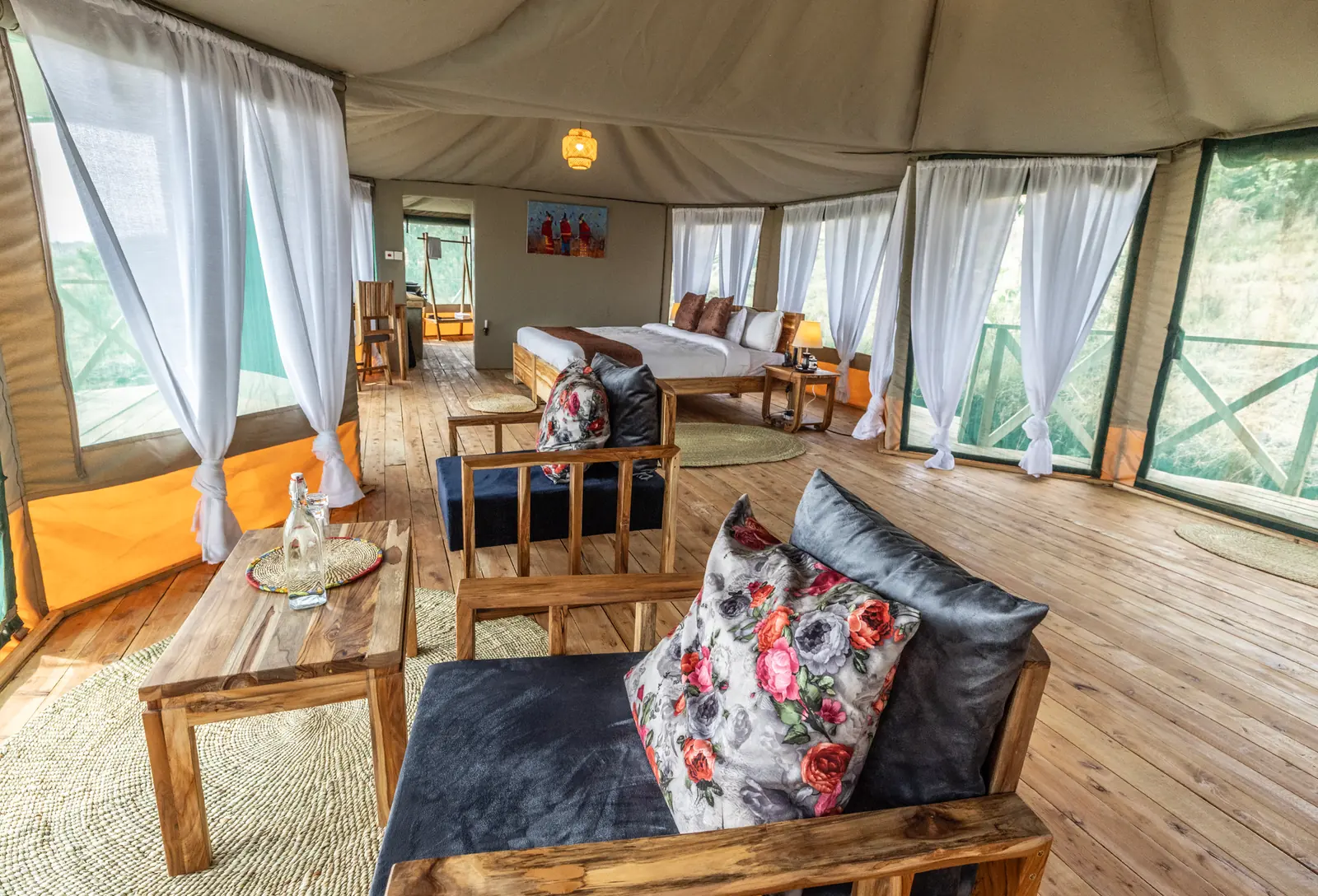 A sofa and armchair in a tent, with the double bed behind under the canvas roof
