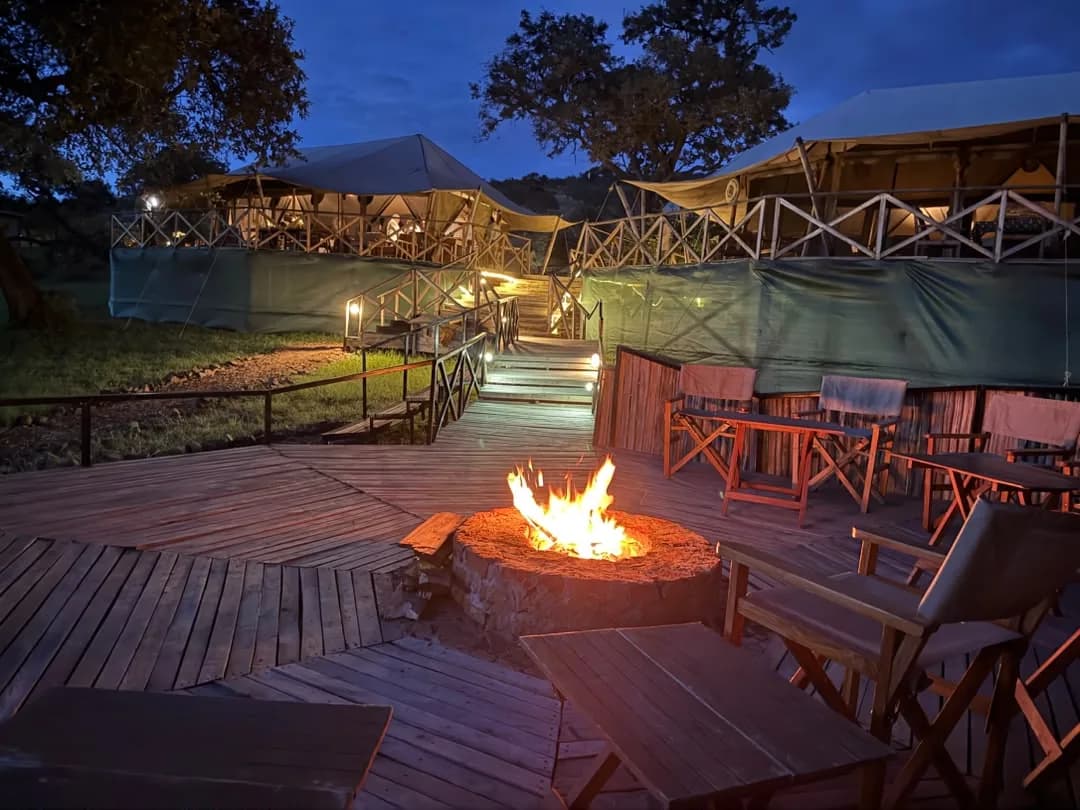 A fire burning in the deck fire pit at dusk, below the lit main tents