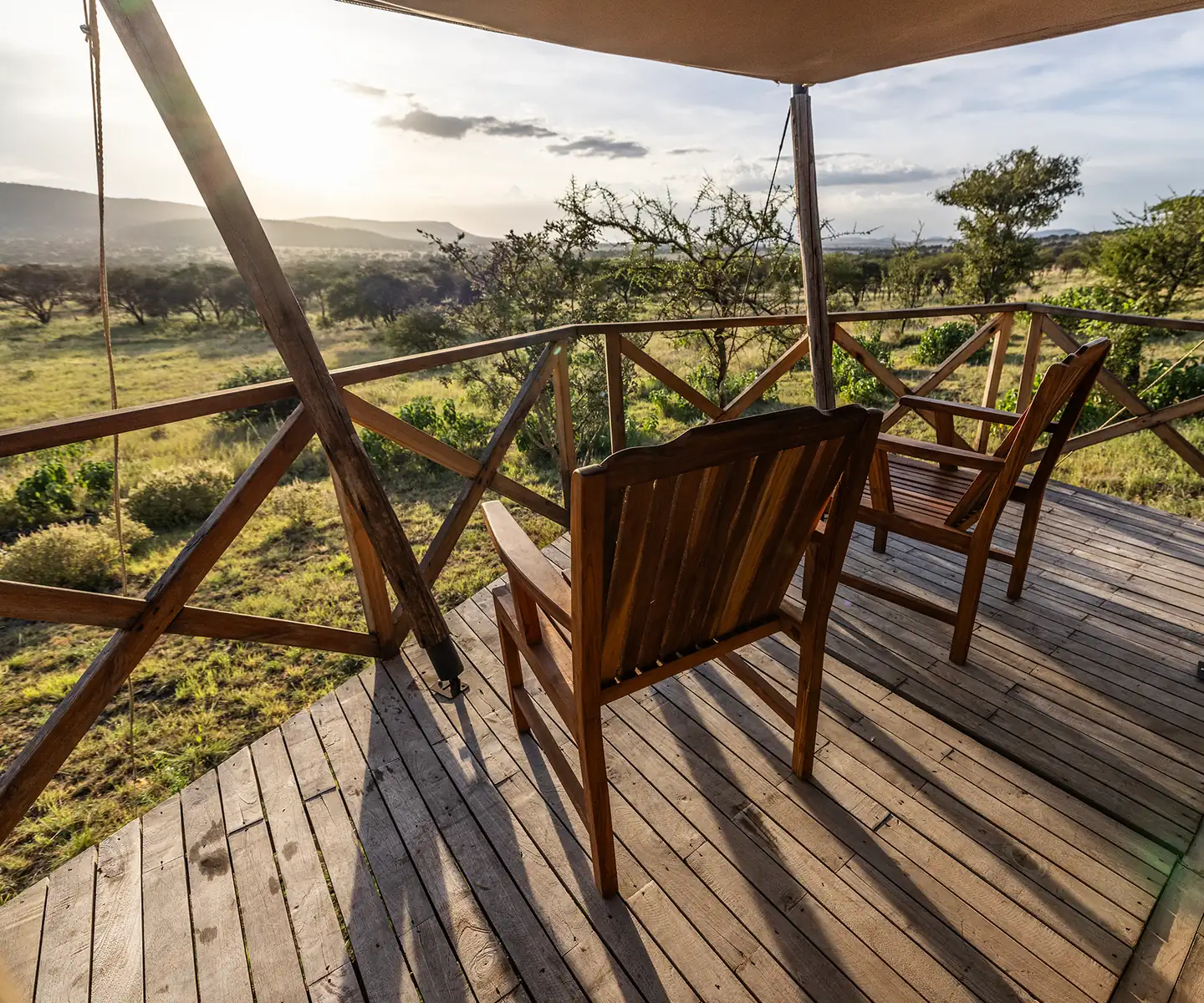 Two wooden chairs on a tent veranda, looking out over green bush in the morning sun