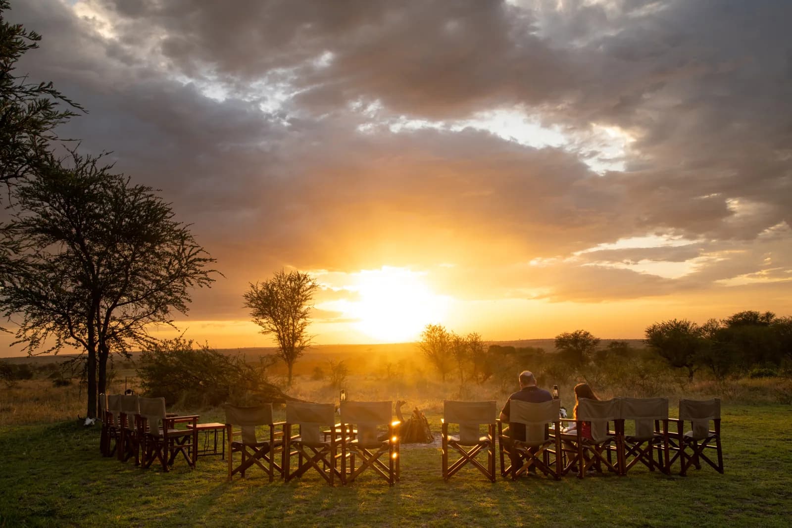 Guests in camp chairs as the sun sets over the plains at Serengeti Kati Kati