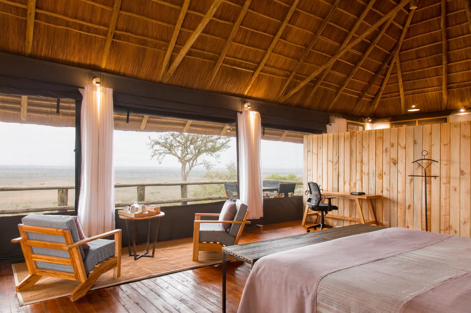 Bedroom with armchairs and a wide window over the plains, under a thatched roof
