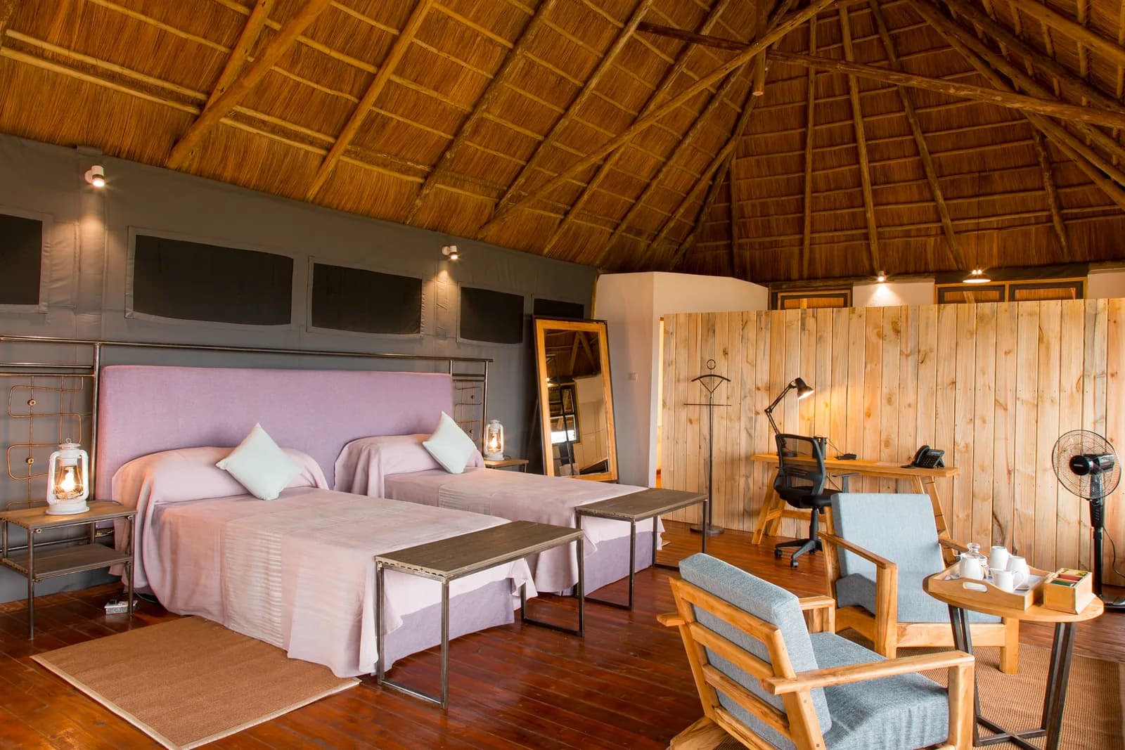 Twin beds, armchairs and a desk under a thatched roof