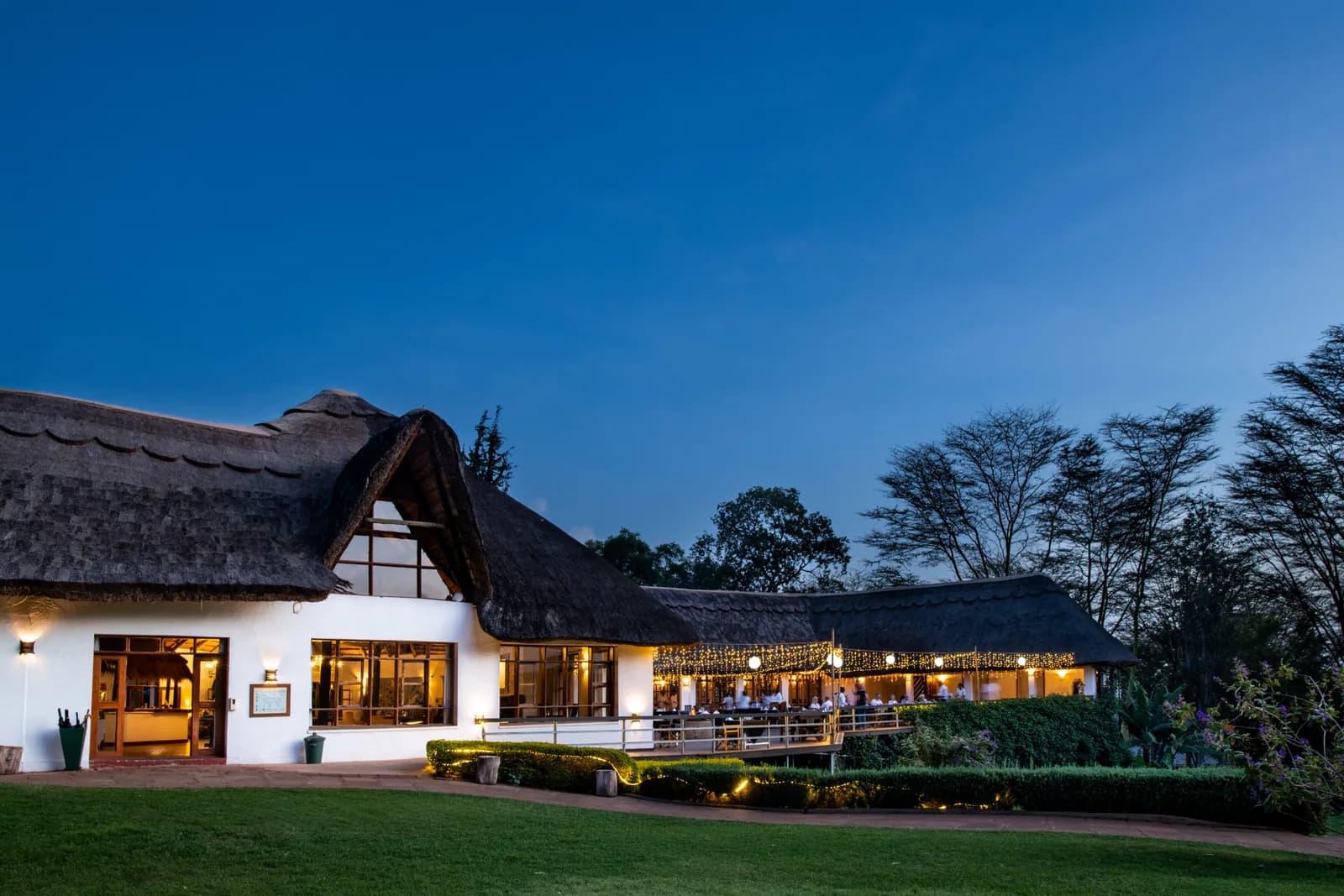 The thatched Ngorongoro Farm House and its lawn, lit up at dusk