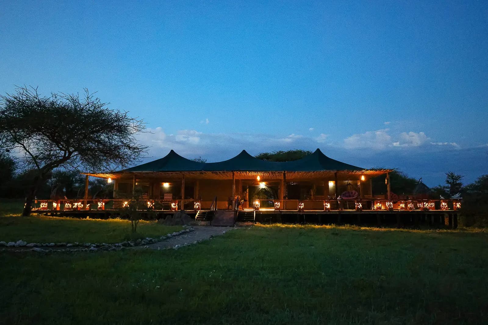 The main tent of Serengeti Sound of Nature lit up at dusk across the lawn