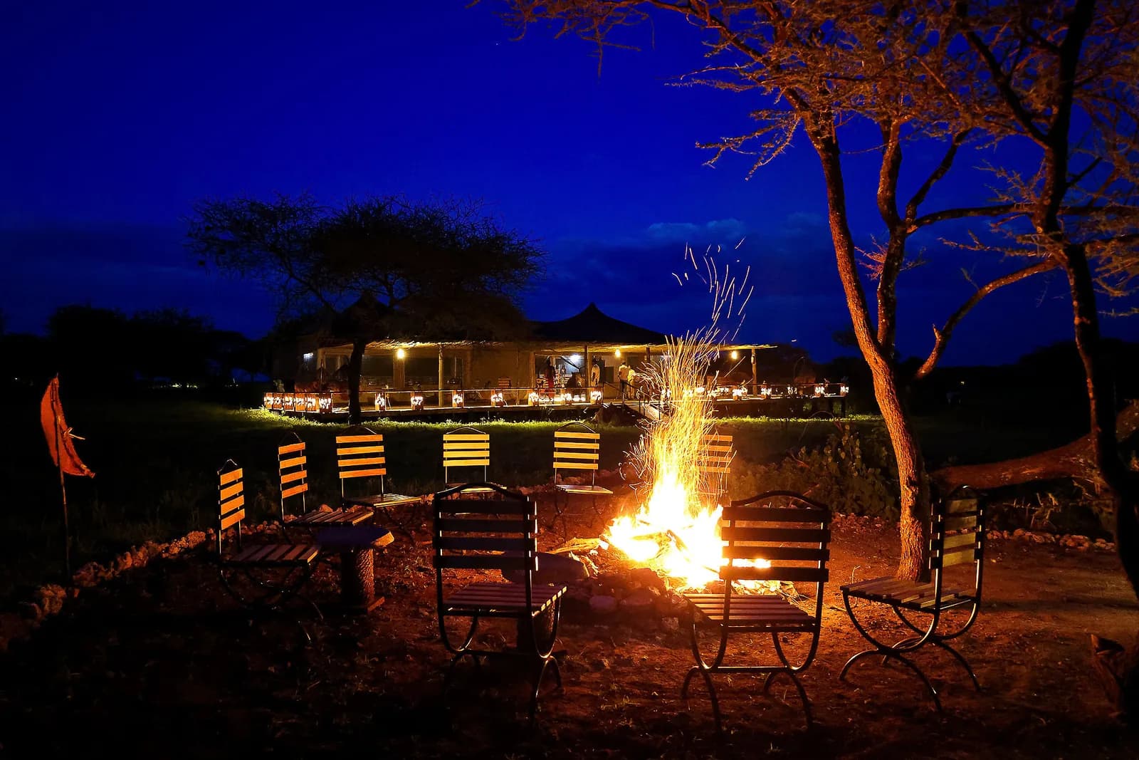 Campfire with chairs around it at night, the main tent lit behind