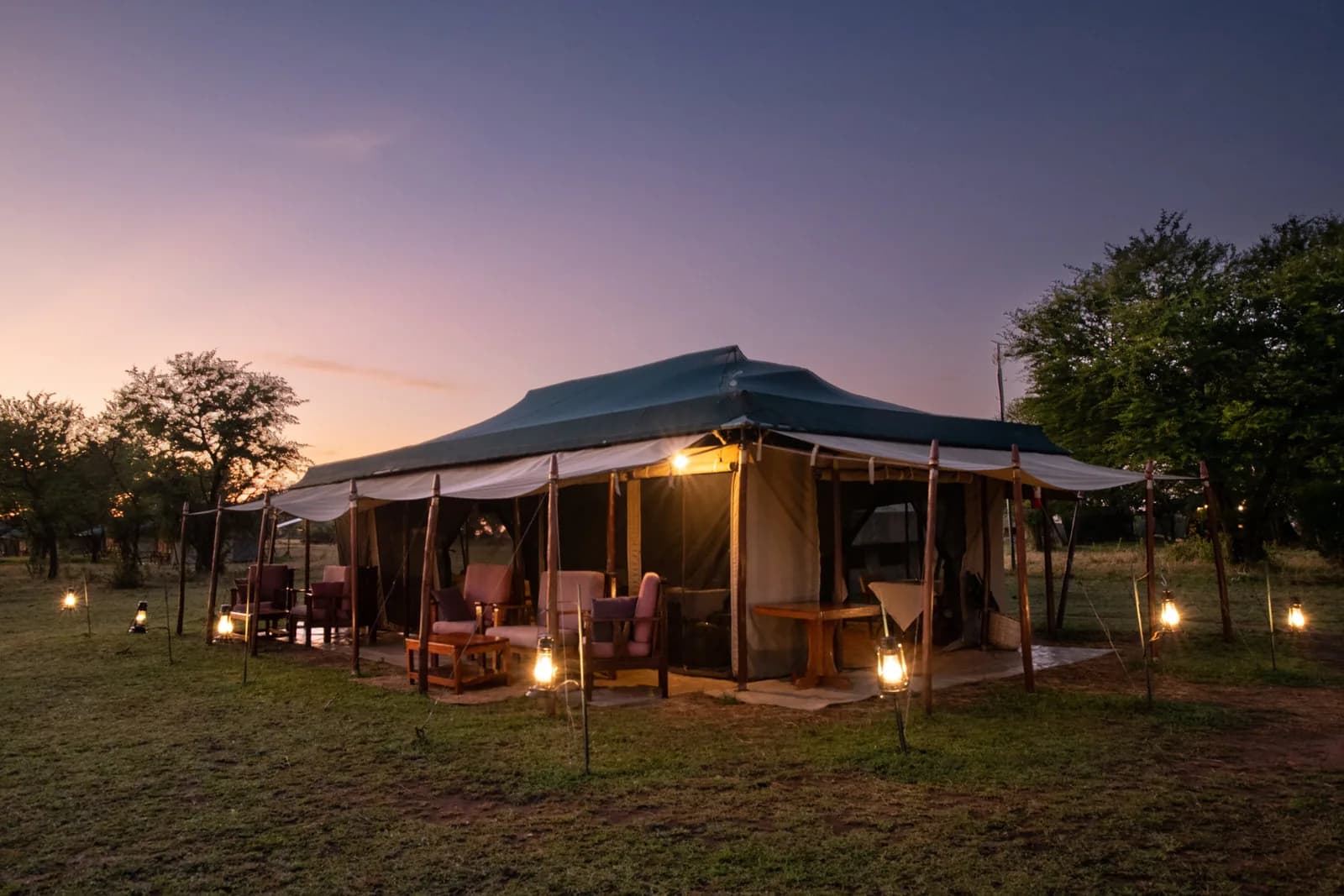 A tent lit up at dusk, with lanterns on the grass