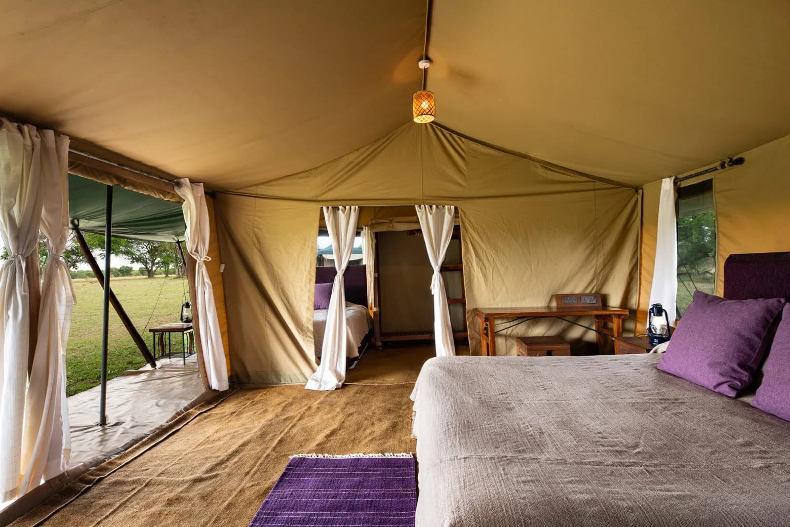 Double bed with purple cushions in a tent, the bathroom behind