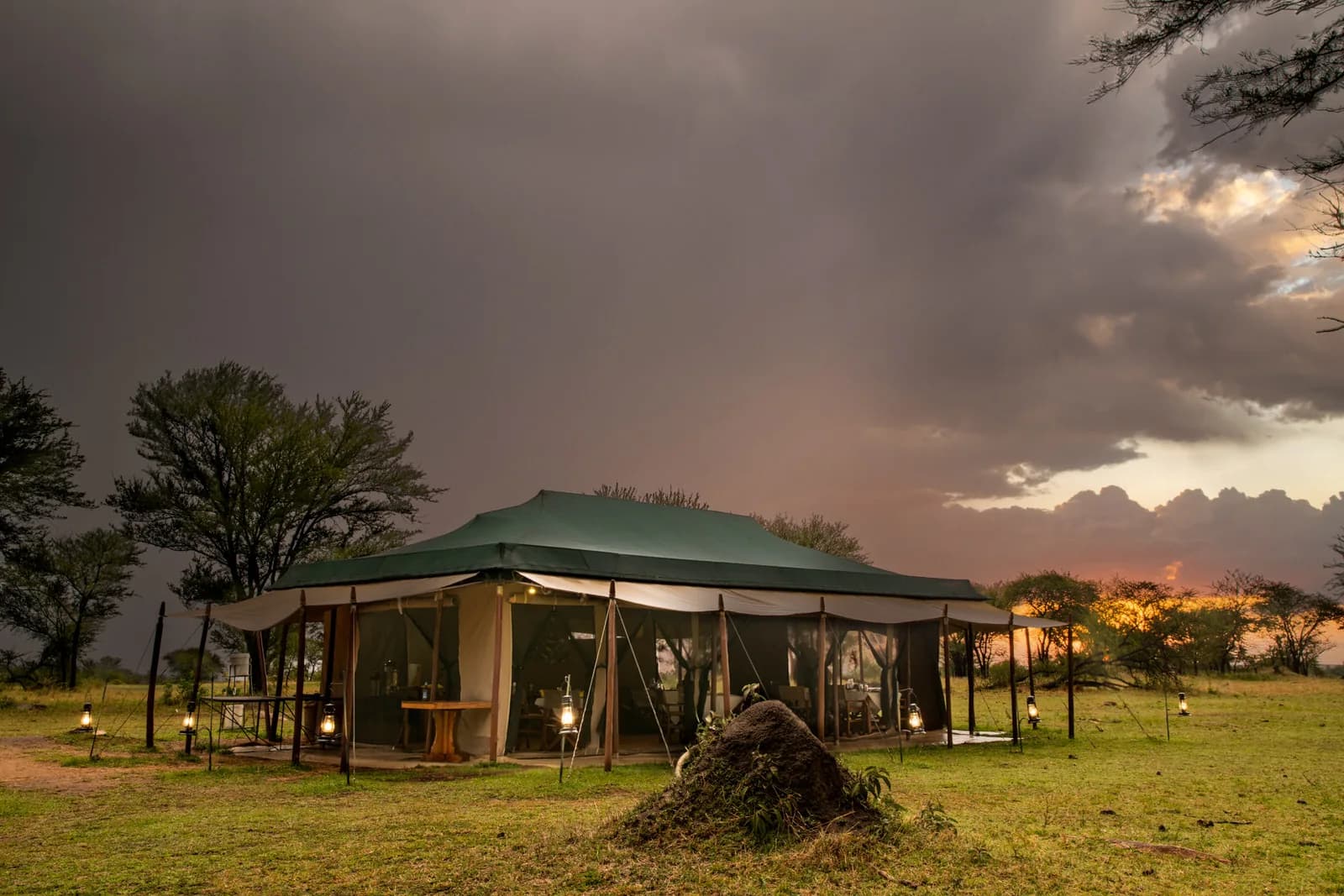 A tent lit by lanterns on the open plains under a stormy evening sky