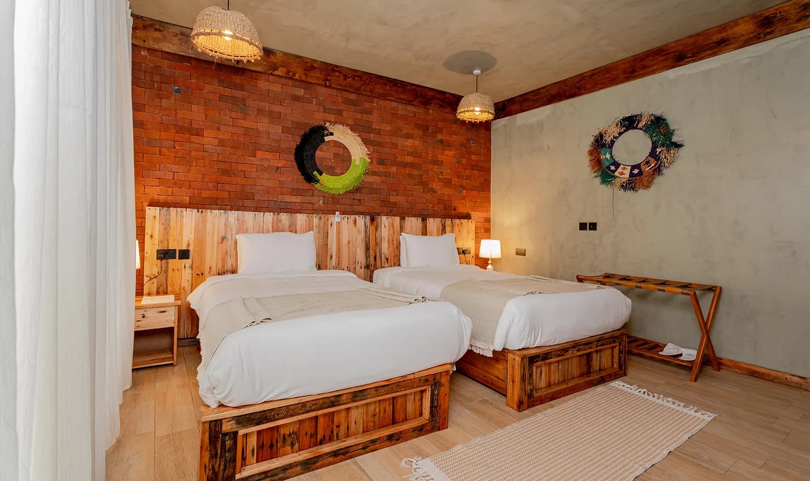 A twin room with a red-brick wall, wooden bed frames and woven wall hangings