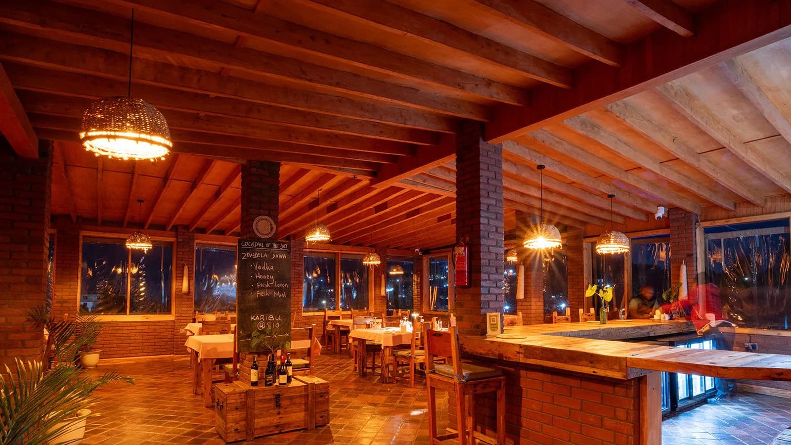 The restaurant and bar under a timber ceiling, with brick pillars, hanging basket lamps and laid tables