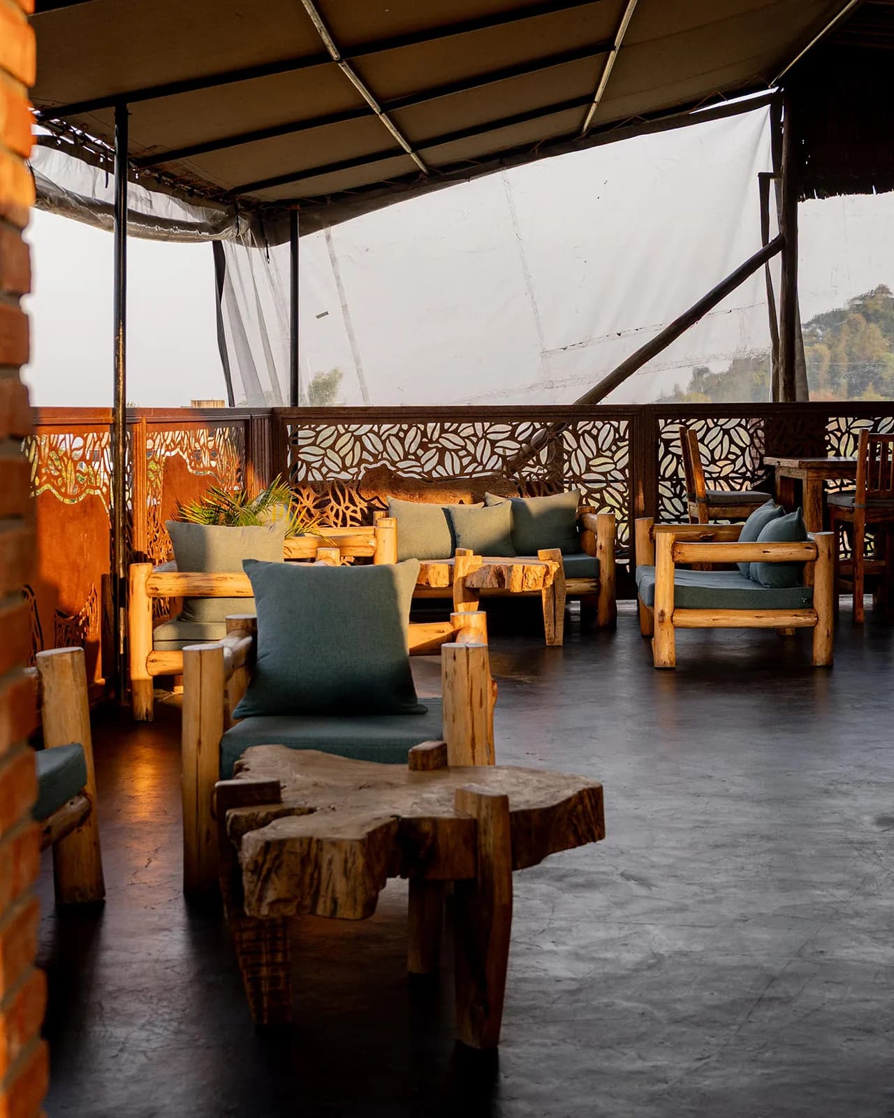A covered rooftop lounge with wooden sofas, cushions and a tree-trunk coffee table