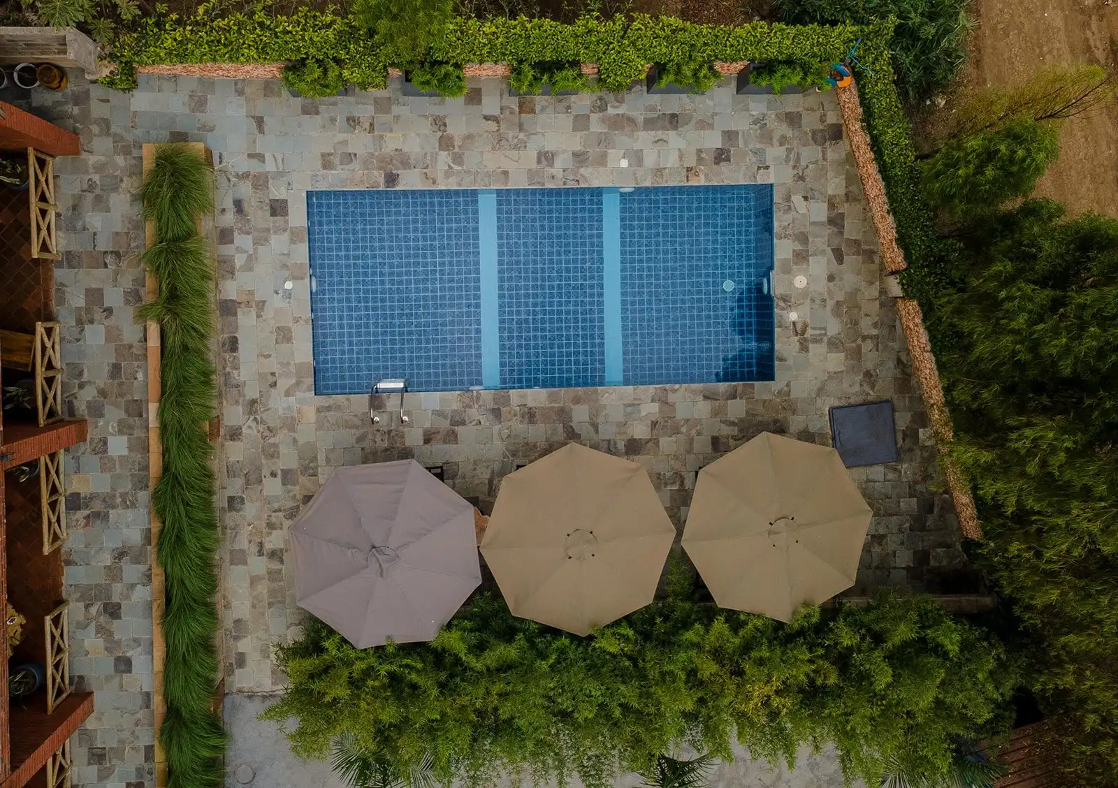 An overhead view of the pool, the stone terrace and three open umbrellas