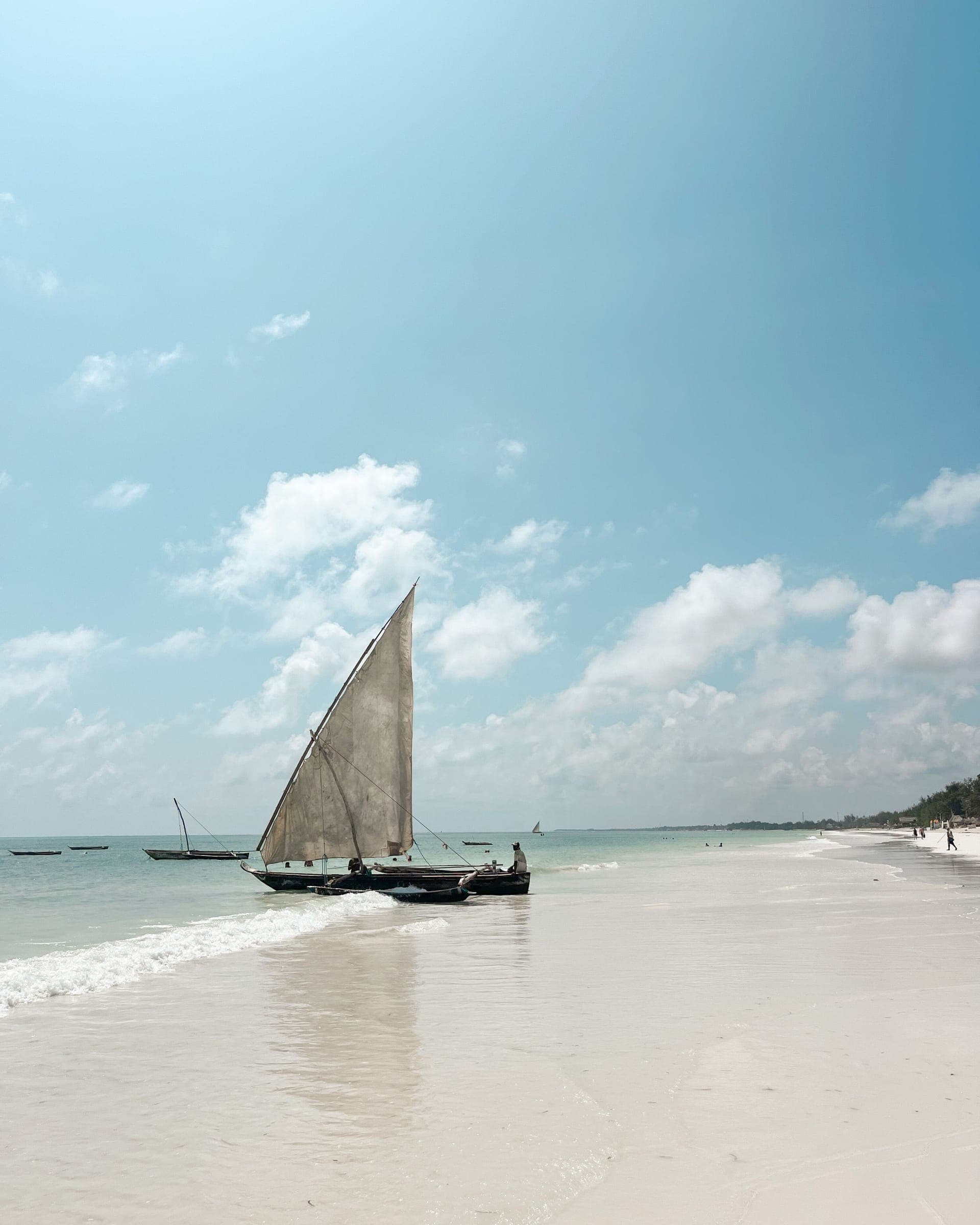 A traditional dhow with a canvas sail drawn up on white sand