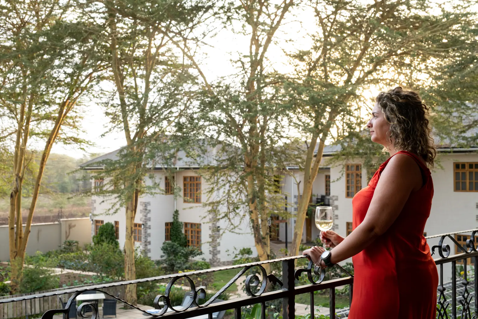 A guest with a glass of wine on a balcony overlooking the gardens
