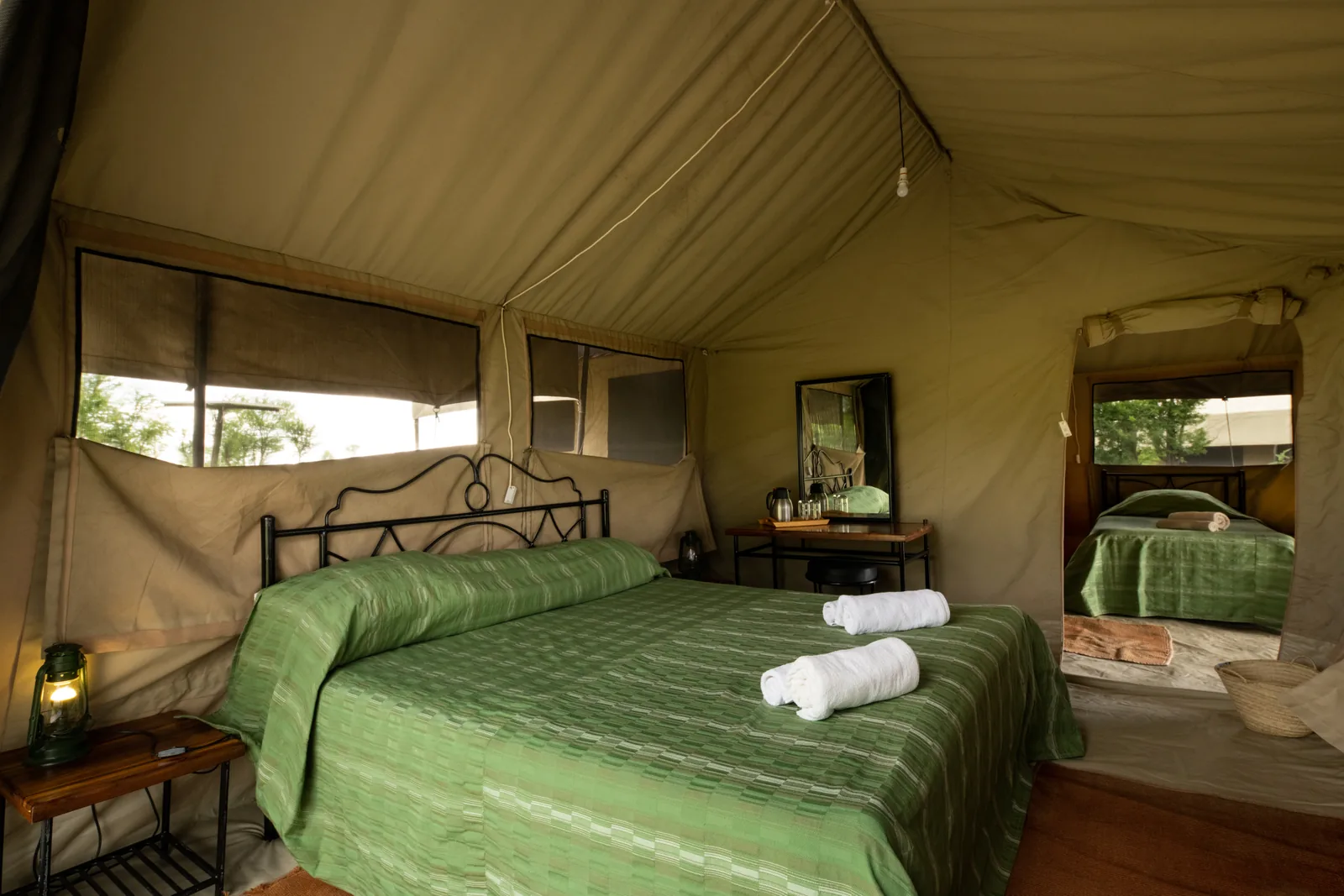 Double bed and lantern in a tent, with the bathroom behind