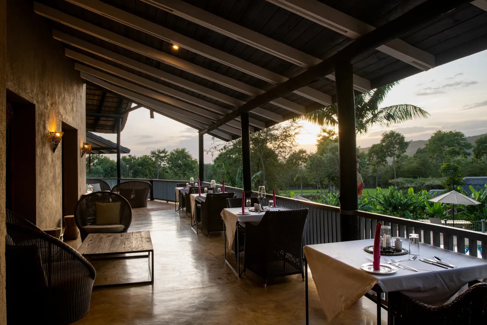 Veranda restaurant with tables set, the sun low over the garden