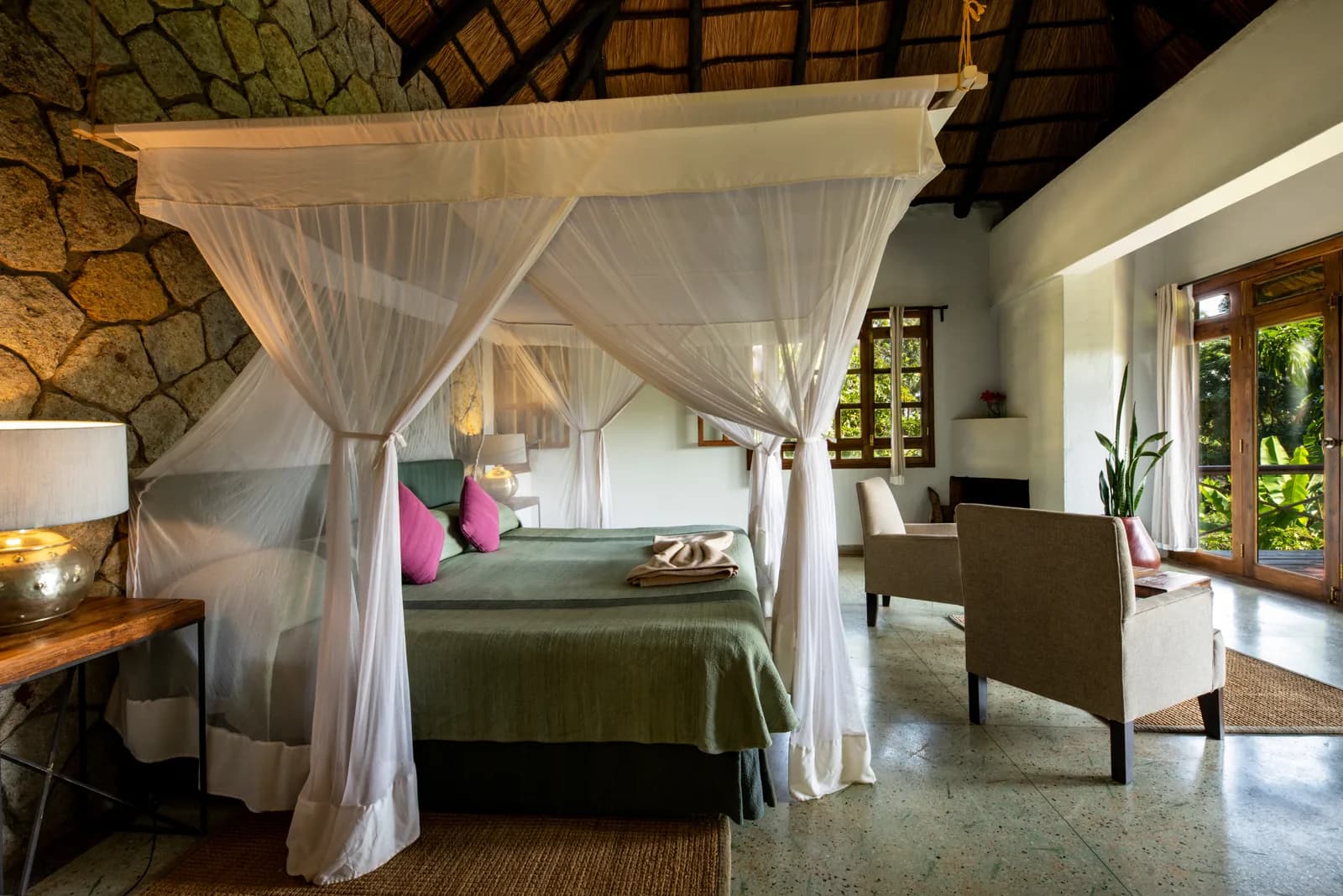 Four-poster bed with white nets beside a stone wall