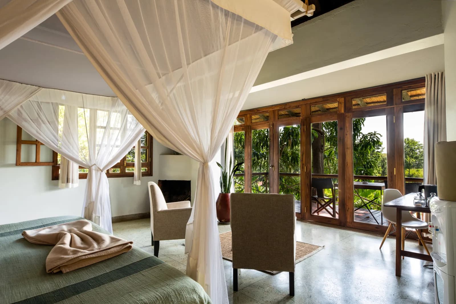 Netted four-poster bed and armchairs by glass doors to a balcony