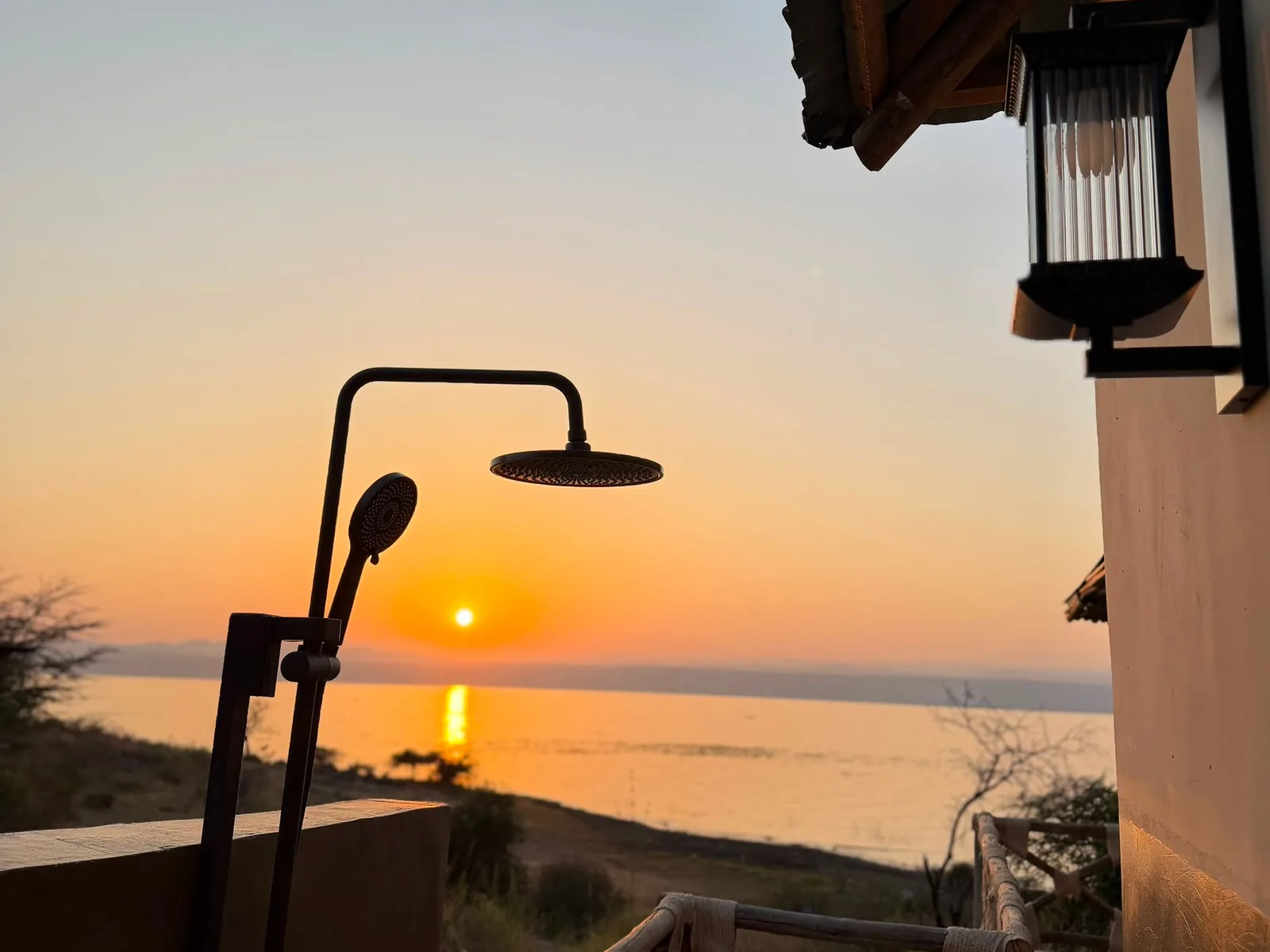 Outdoor shower on a terrace, with the sun setting over the lake beyond