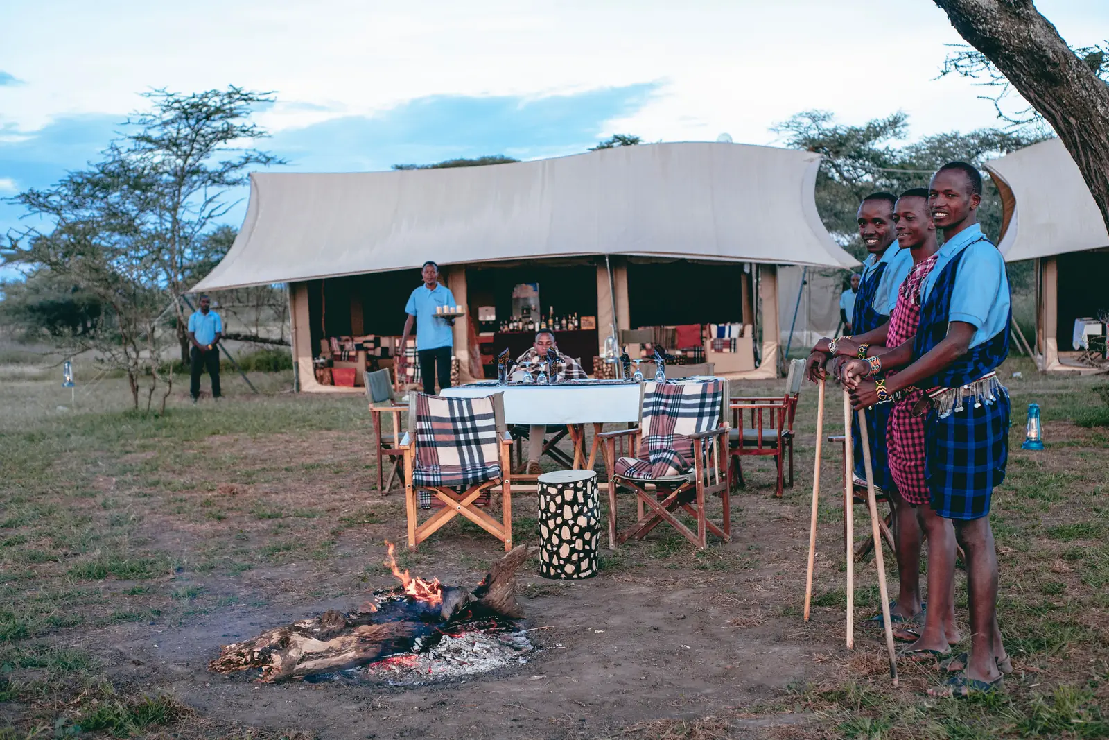 Maasai staff with spears beside a campfire in front of the dining tent
