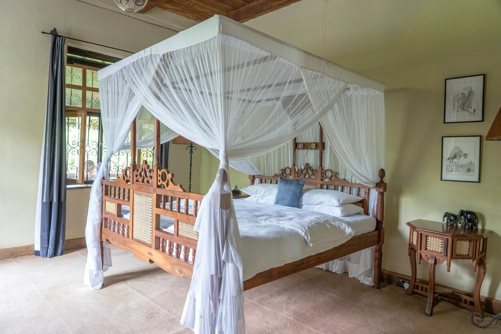 A carved wooden four-poster bed under a white mosquito net, with framed wildlife drawings on the wall
