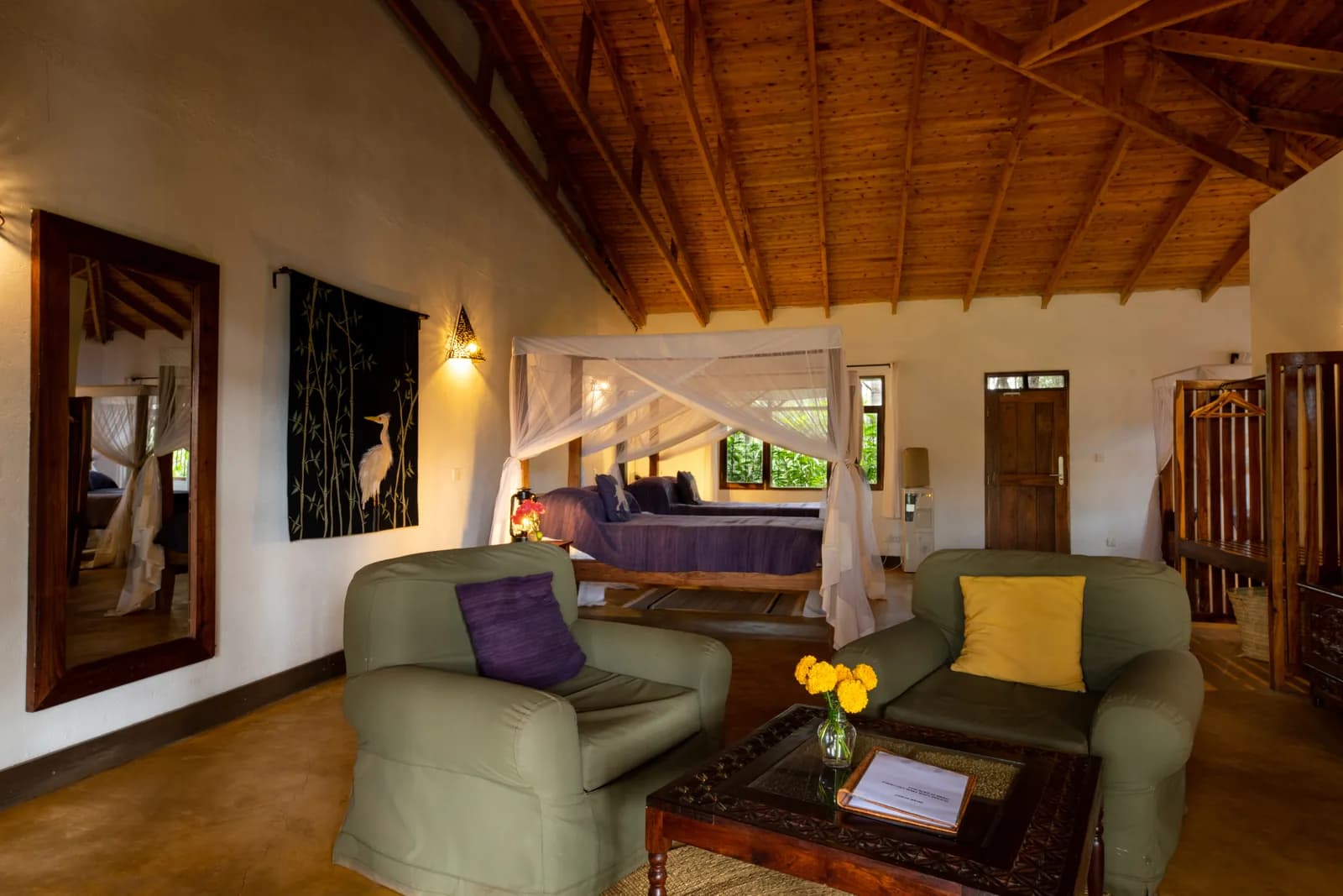 Sitting area with armchairs and a four-poster bed under a timber roof