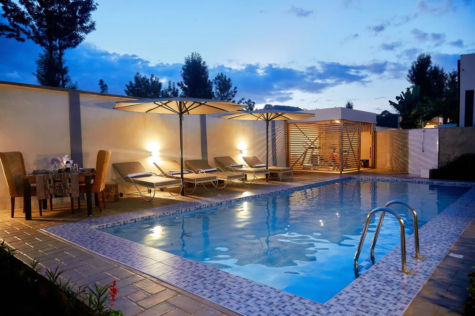 Lit swimming pool with loungers and parasols at dusk