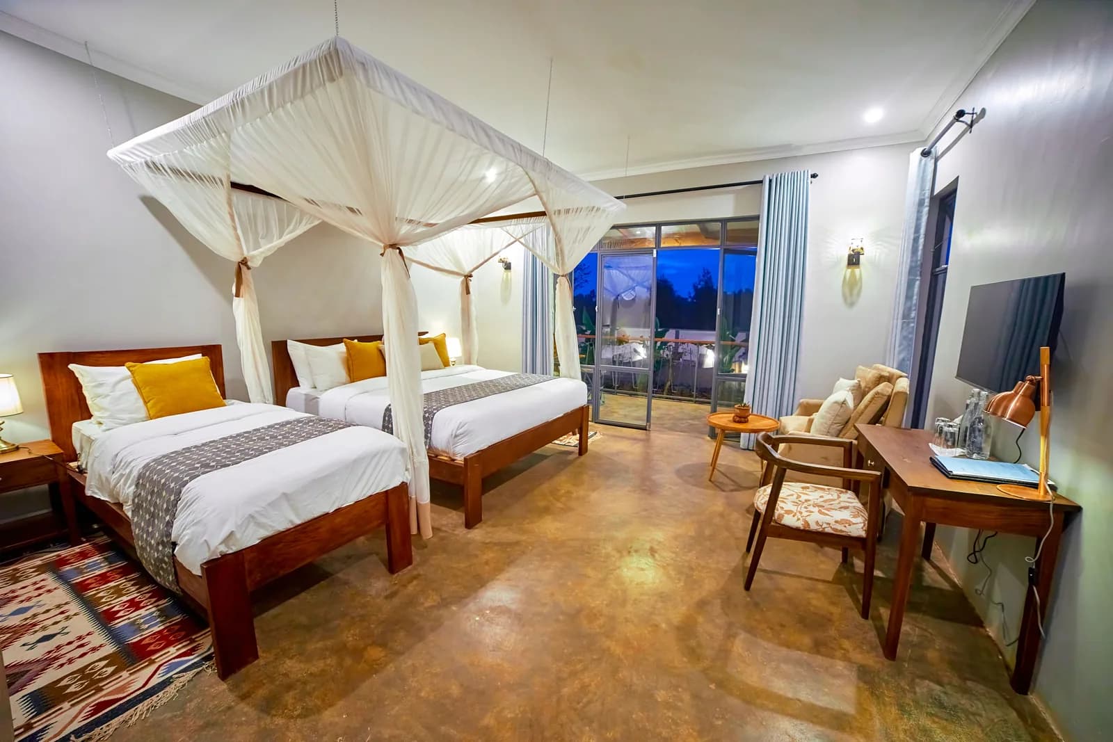 Twin beds under mosquito nets, with a desk and glass doors