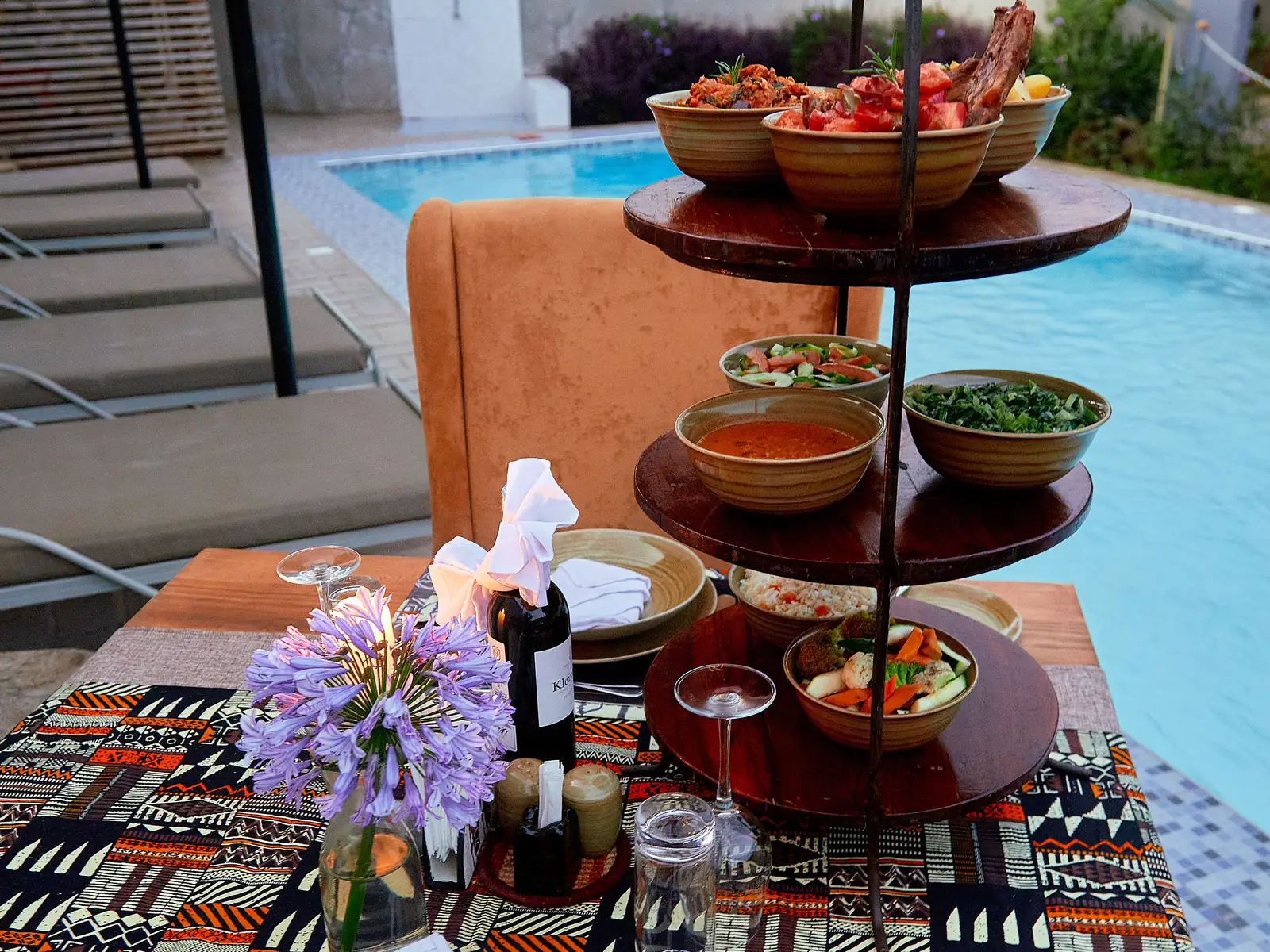 A tiered stand of food on a table by the pool