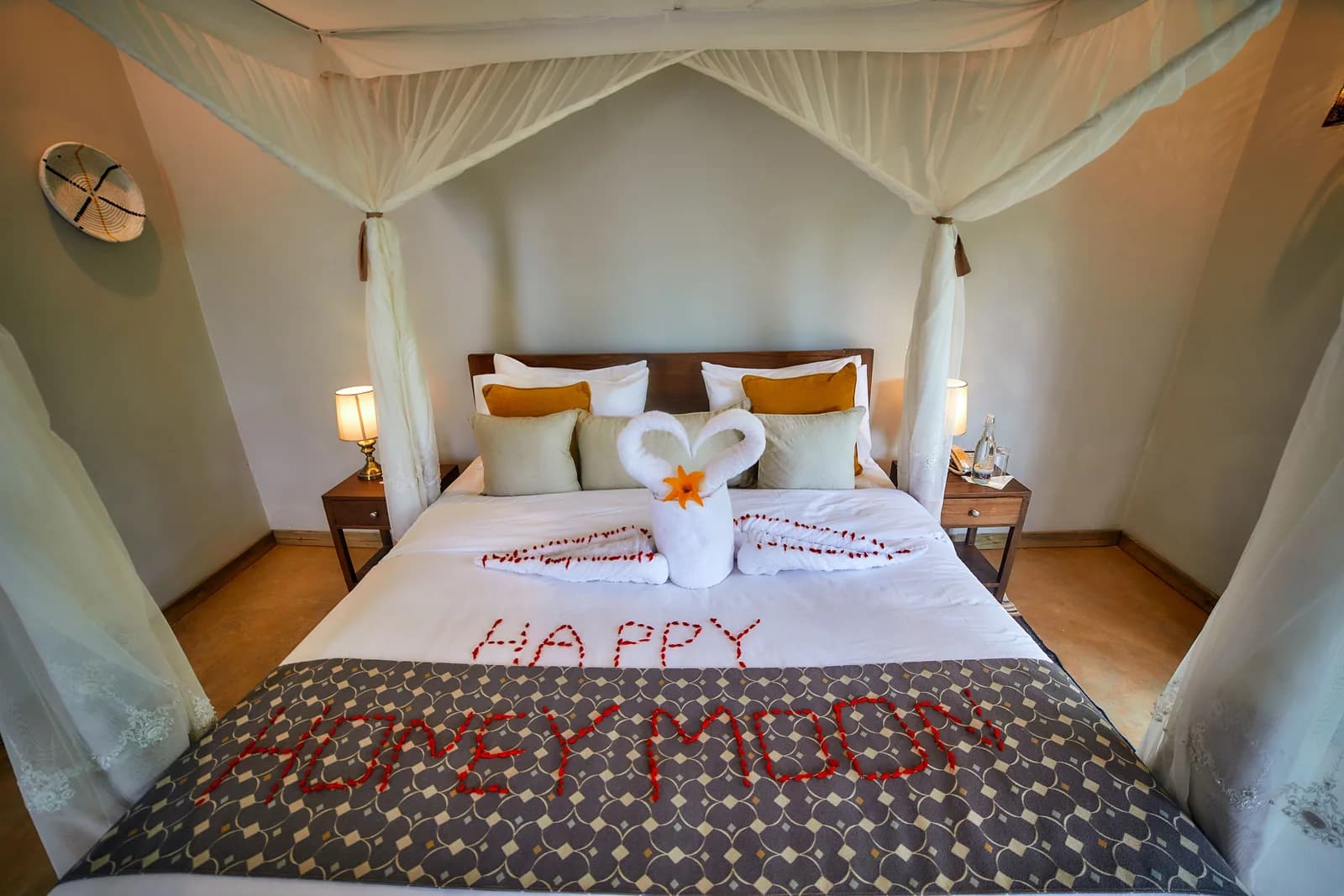 A four-poster bed under a mosquito net, with towel swans and Happy Honeymoon spelt out in petals