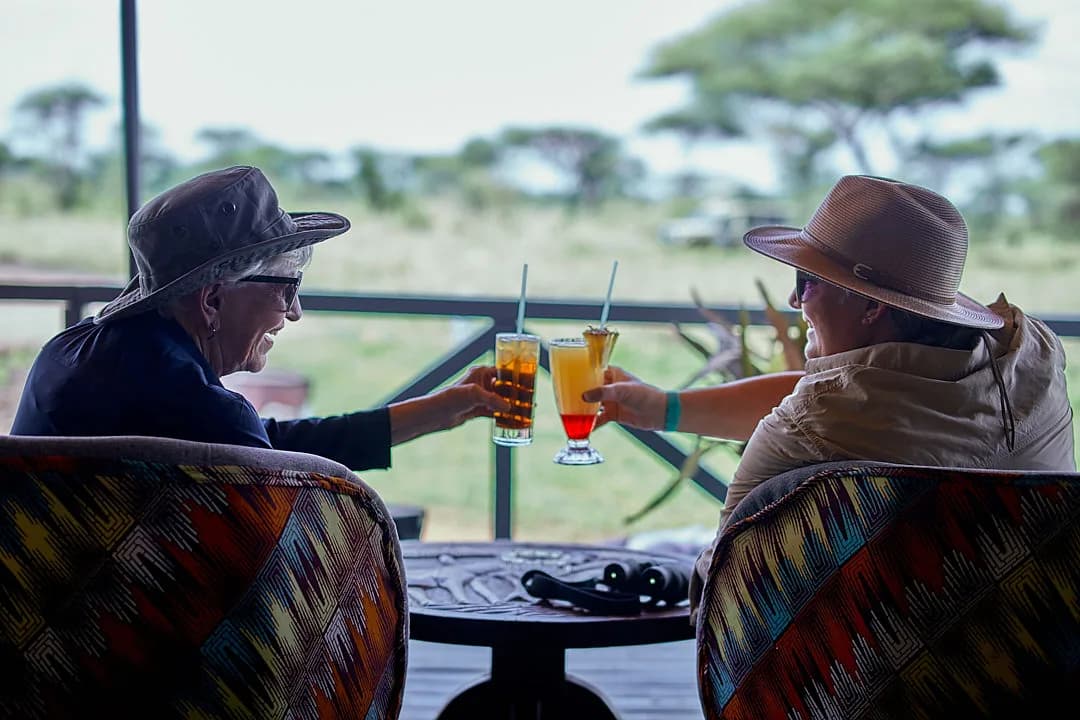 Two guests raising drinks on a deck looking over the plains