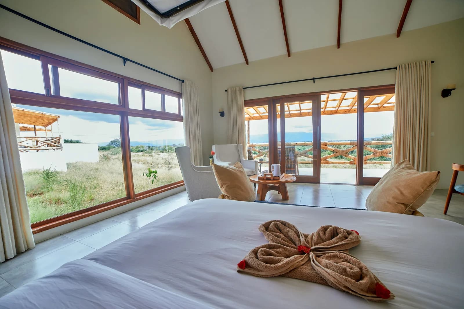 Bed with a towel flower, and floor-to-ceiling windows onto the bush